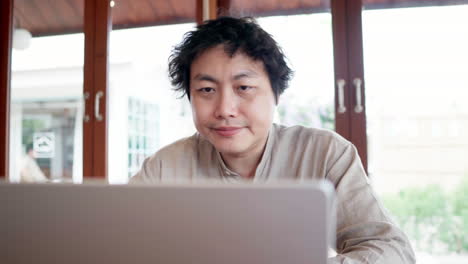 Fokussierter-Asiatischer-Mann,-Der-Tagsüber-Im-Café-Auf-Einen-Silbernen-Laptop-Schaut
