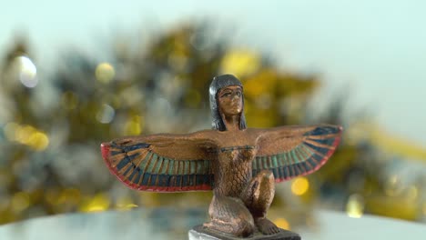 Verträumte-Nahaufnahme-Einer-Kleopatra-Statue-Mit-Weit-Geöffneten-Flügeln,-Verschwommener-Goldener-Schärfentiefe,-Antiker,-ägyptischer-Historischer-Herrscher,-Antikes-Kunstwerk-Einer-Göttin,-Rotierendes-360-Kino-4K-Video-Nach-Oben-Geneigt