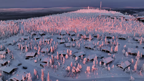 Aerial-tracking-shot-of-cabins-on-top-of-the-Iso-Syöte-fell,-winter-sunrise-in-Finland