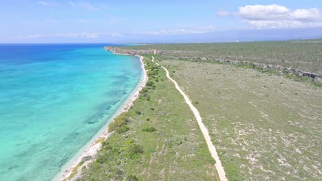 Aerial-forward-flight-over-green-island-with-path-along-sandy-beach-and-turquoise-Caribbean-sea---Bahia-de-las-Aguilas,-Pedernales