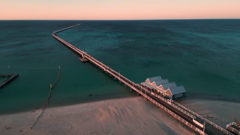 revealing-drone-shot-of-the-Busselton-Jettty,-the-longuest-jetty-in-the-southern-hemisphere,-with-the-beautiful-colors-of-the-sunset