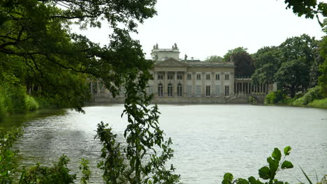 El-Palacio-En-La-Isla-De-Varsovia:-Un-Majestuoso-Palacio-Neoclásico-Junto-Al-Lago,-Enmarcado-Por-Frondosos-árboles,-Que-Refleja-Tranquilidad-Y-Elegancia-Histórica