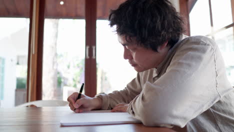 Hombre-Asiático-Escribiendo-Un-Plan-De-Ideas-En-Un-Cuaderno-En-Una-Cafetería