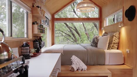 Cinematic-slider-going-across-timber-tiny-cabin-with-luxury-furnishings-and-large-floor-to-ceiling-windows-looking-out-to-the-national-park