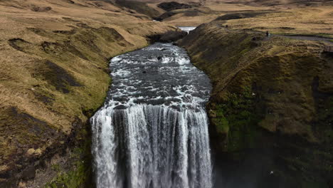 Aerial-view-backwards-over-the-Skogafoss-waterfall,-cloudy,-fall-day-in-Iceland