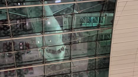 Passengers-Disembarking-an-Airplane-Through-Jet-Bridge,-Emirates-Airlines-Jet-Plane-at-Dubai-Airport-at-Night---View-Through-the-Windows-of-Airport-Terminal