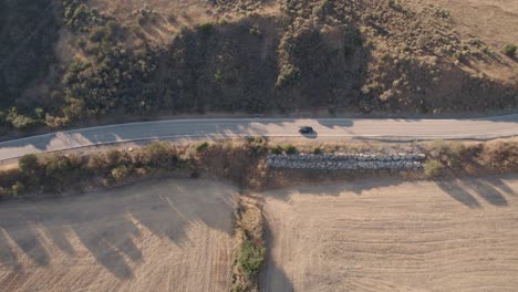 Aerial-view-of-a-car-driving-on-a-road-through-fields-of-harvested-crops