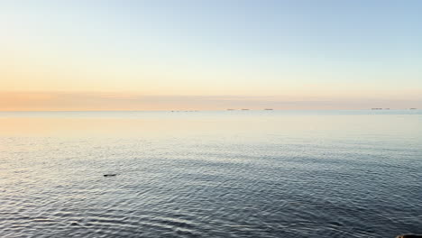 The-sea-mirrors-the-soft-hues-of-dusk,-offering-a-tranquil-vista-with-distant-ships-on-the-horizon