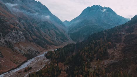 Flying-on-Malojapass-in-Switzerland-following-the-mountain-river-towards-the-big-mountain-in-autumn-in-a-moody-setting