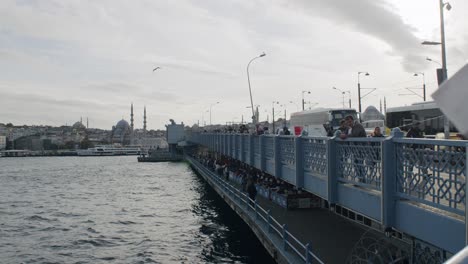 Fishermen-on-the-famous-Galata-Bridge-fishing-with-view-of-The-New-Mosque-in-background