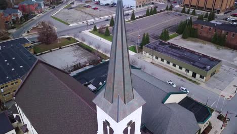 Aerial-view-rising-up-quaint-Logansport-church-steeple,-cross-and-bell-tower,-Indiana