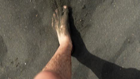 Man-walking-barefoot-on-black-sand-beach,-POV-view
