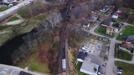 Aerial-view-following-industrial-train-travelling-through-Logansport-Indiana-idyllic-autumn-neighbourhood