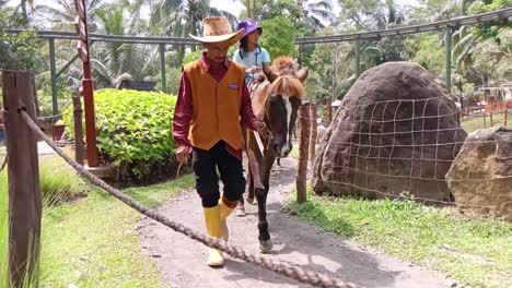 Little-Girls-riding-horses-guided-by-staff-at-a-playground-in-the-countryside,-Semarang,-Central-Java