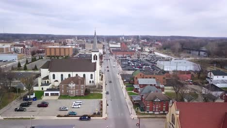 Aerial-view-flyover-Logansport-downtown-street-towards-small-white-church-with-steeple-in-Indiana-townscape