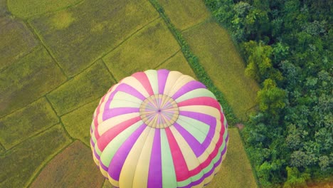 Looking-Down-At-Top-Of-Colourful-Hot-Air-Balloon-Flying-Over-Green-Fields-In-Vang-Vieng,-Laos