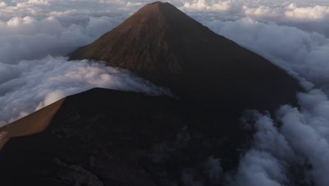 Reveal-shot-of-Fuego-volcano-surrounded-by-morning-clouds,-aerial