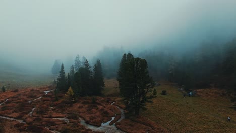 Überflug-Der-Farbenfrohen-Herbstlichen-Bergregion-In-Der-Schweiz-über-Nebelverhangene-Tannen-Den-Fluss-Hinunter,-Wo-Wanderer-Nach-Einer-Berghütte-Suchen