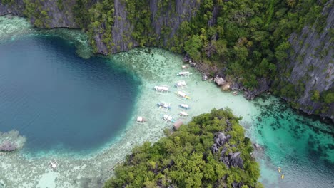 Tour-boats-and-blue-hole-at-twin-lagoon-amid-towering-karst-and-clear-water,-coron
