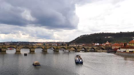 Ferries-on-the-Vltava-River-passing-under-the-Charles-Bridge,-Prague,-Czech-Republic