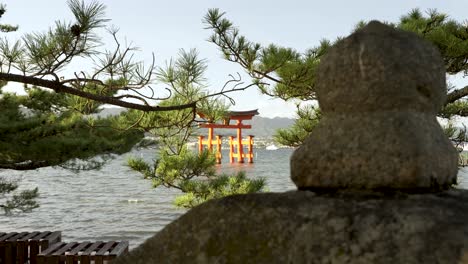 Schwimmendes-Grand-Torii-Tor-Bei-Sonnenuntergang-Im-Hintergrund-Bei-Itsukushima,-Betrachtet-Durch-Kiefernzweige-Im-Vordergrund