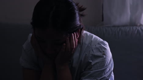 Distressed-depressed-woman-with-hand-on-face-and-neck-crying-in-dark-room