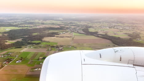 Goldener-Sonnenuntergang-Aus-Einem-Flugzeugfenster,-Mit-Dem-Flugzeugmotor-über-Einer-Pastoralen-Landschaft