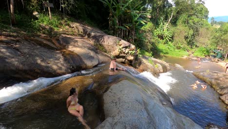 Happy-male-tourist-slides-down-famous-waterfall-Mo-Pang,-refreshment-and-fun