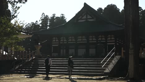 Couple-Walking-Up-Stairs-Towards-Courtyard-At-Garan-Koyasan's-central-temple-complex-with-view-of-Kondo-Hall-In-background,-Stopping-To-Take-Photo