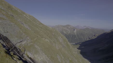 Die-Drohne-Fängt-Zwei-Wanderer-Ein,-Die-Während-Der-Goldenen-Stunde-Auf-Einem-Pfad-Entlang-Des-Steilen-Grashangs-Eines-Berges-Gehen,-Und-Zeigt-Die-Warme-Und-Bezaubernde-Alpenlandschaft