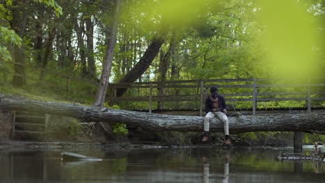 Man-in-the-woods-seated-on-a-tree-trunk-bridge-reflecting-over-water
