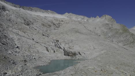 El-Dron-Sube-Sobre-Un-Lago-Glacial-único-Con-Un-Río-Que-Fluye-Sobre-Piedras-De-Granito,-Formado-Por-El-Glaciar-Neves-Visible-Al-Fondo