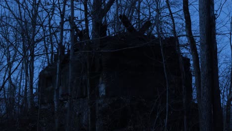 Broken-down-abandoned-hut-with-collapsed-roof-in-autumn-bare-tree-spooky-woodland-at-night