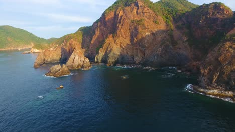 Flying-low-over-the-water-along-the-rocky-cliffs-at-Carrizal-anchorage-near-Manzanillo,-Mexico-just-before-sunset