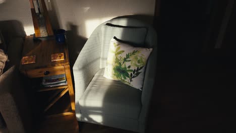 Umlaufende-Aufnahme-Eines-Hellblauen-Stuhls-Mit-Kissen-Im-Wohnzimmer-Eines-Hauses,-Halblicht-Durch-Sonnenlicht,-Das-Durch-Das-Fenster-Strahlt