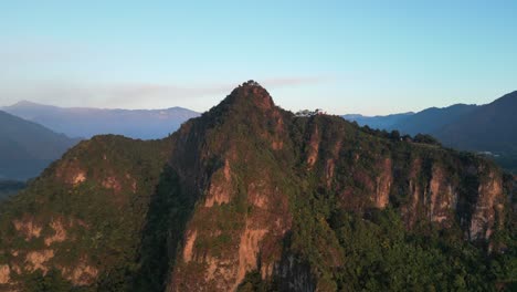 Vista-De-Drones-En-Guatemala-Volando-Frente-A-Una-Montaña-Verde-Rodeada-De-Volcanes-Al-Amanecer-En-Atitlán