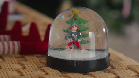 Snow-globe-with-a-festive-figurine-and-Christmas-tree-on-a-woven-mat