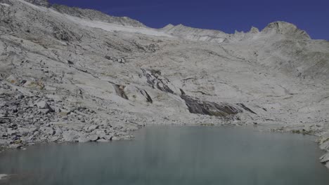 Drohne-Klettert-über-Einen-Einzigartigen-Gletschersee-Mit-Einem-Fluss,-Der-Auf-Granitsteinen-Fließt-Und-Im-Hintergrund-Vom-Neves-Gletscher-Geformt-Wird