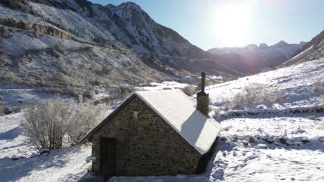 aerial-shot-of-a-lonely-snowy-rustic-house-in-the-middle-of-the-mountains-of-a-valley-in-the-Spanish-Pyrenees-in-a-sunny-day-with-the-door-open