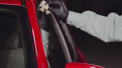 Engineer-wearing-black-gloves-and-using-green-microfiber-cloth-to-clean-up-red-car-side-window-mirror