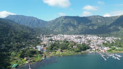 Drone-view-in-Guatemala-flying-over-a-blue-lake-surrounded-by-green-mountains-and-volcanos-and-a-town-on-a-sunny-day-in-Atitlan