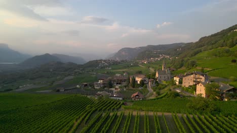 Die-Drohne-Erfasst-Das-Dorf-Pinzano-In-Südtirol-Zur-Goldenen-Stunde,-Mit-Dem-Montagna-Dorf-Im-Hintergrund