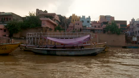 Cinematic-slow-motion-Varanasi-India-Ganges-River-cruise-canal-boats-Northern-State-large-gathering-at-shore-Ancient-Holy-city-Ghat-Pradesh-Province-landscape-gray-cloudy-afternoon-muddy-brown-left