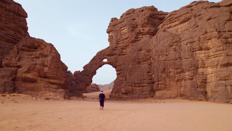 Hombre-Caminando-En-El-Desierto-En-El-Parque-Nacional-Tassili-N&#39;ajjer-Hacia-La-Formación-Rocosa-Con-Forma-De-Elefante-En-Argelia