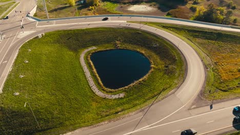 aerial-drone-shot-of-a-highway-overpass-entrance-and-exit-ramp-with-small-pond-in-the-middle-with-cars-moving-on-the-highway-on-a-sunny-day