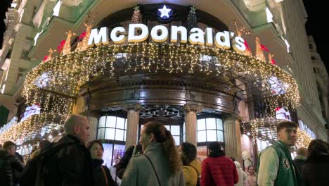 Se-Ve-A-La-Gente-Frente-A-La-Cadena-De-Restaurantes-De-Hamburguesas-De-Comida-Rápida-Multinacional-Estadounidense,-McDonald&#39;s,-Decorada-Con-Luces-Navideñas.