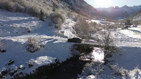 aerial-following-of-car-crossing-a-bridge-of-a-river-in-the-middle-of-the-Spanish-Pyrenees-mountains-surrounded-by-snow