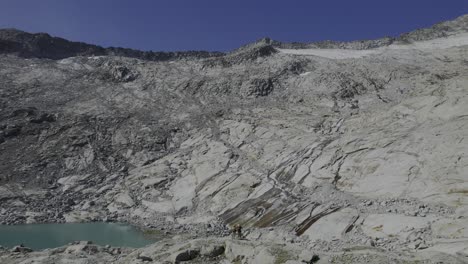 Hikers-admire-a-glacial-lake-and-take-a-picture-of-the,-water-flowing-on-granite-modelled-by-the-glacier