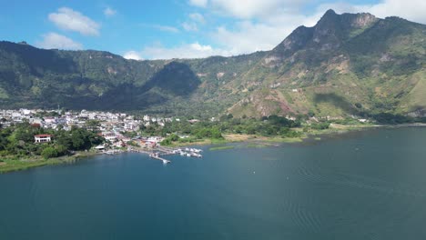 Drone-view-in-Guatemala-flying-over-a-blue-lake-surrounded-by-green-mountains-and-volcanos-on-a-sunny-day-in-Atitlan