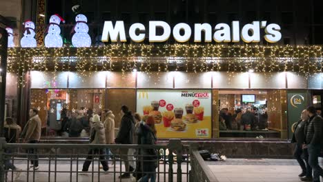Pedestrians-walk-past-the-American-multinational-fast-food-hamburger-restaurant-chain,-McDonald's,-decorated-with-Christmas-lights